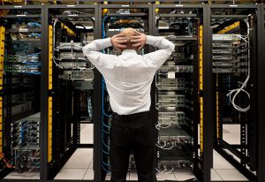 A man stands in front of a server farm with his head held in distress