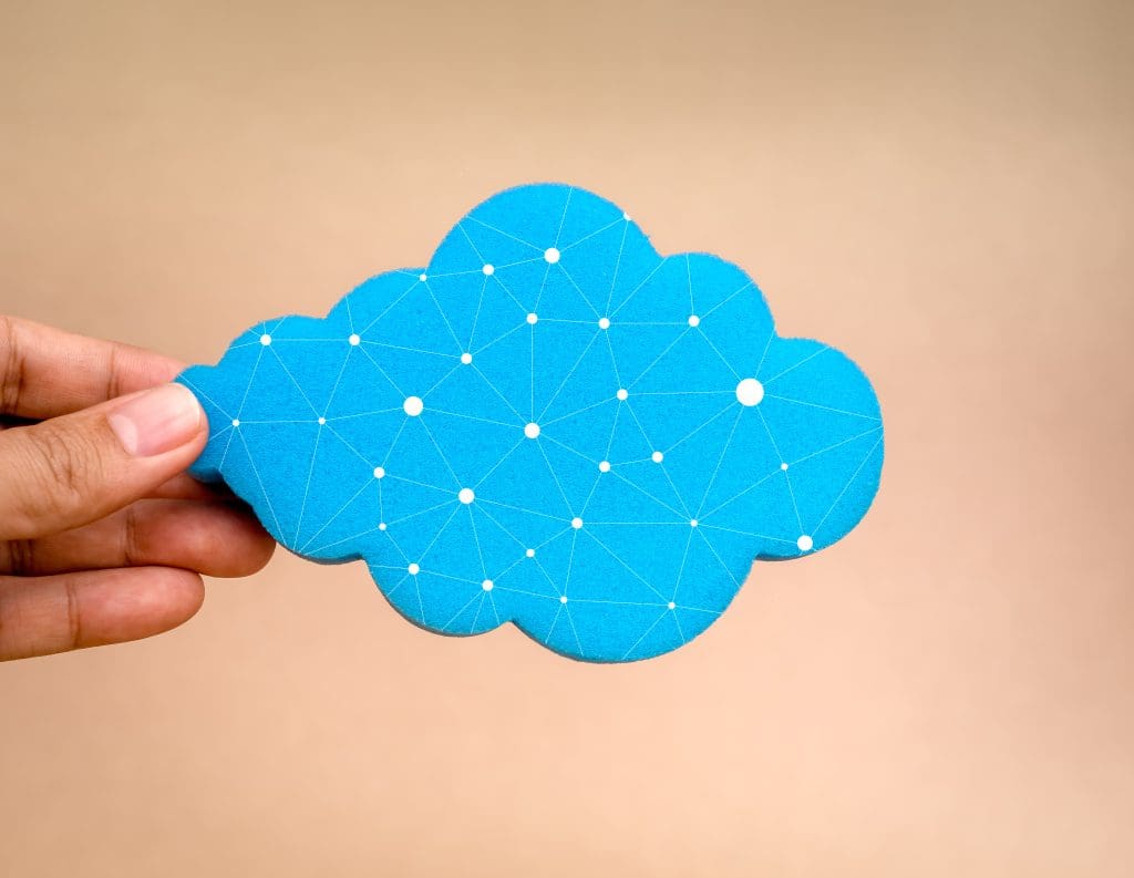 A close-up of a hand holding a cloud-shaped blue sponge with a network of white dots and lines drawn on it.